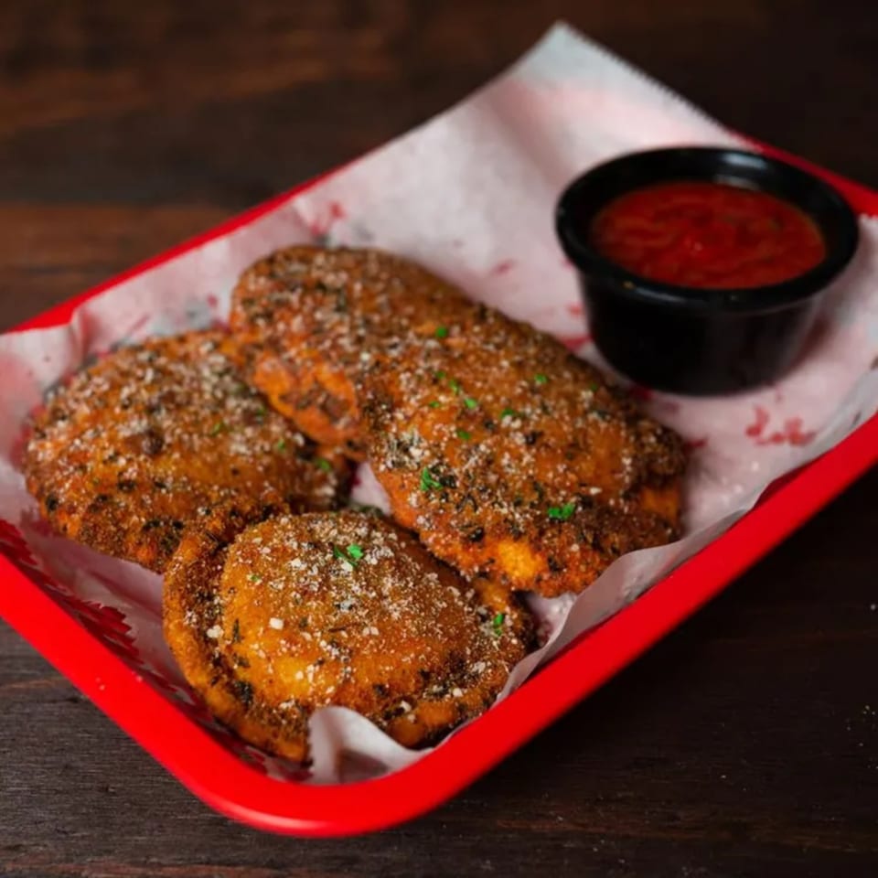 Three golden-brown fried ravioli, sprinkled with Parmesan and herbs, served with a side of marinara sauce.