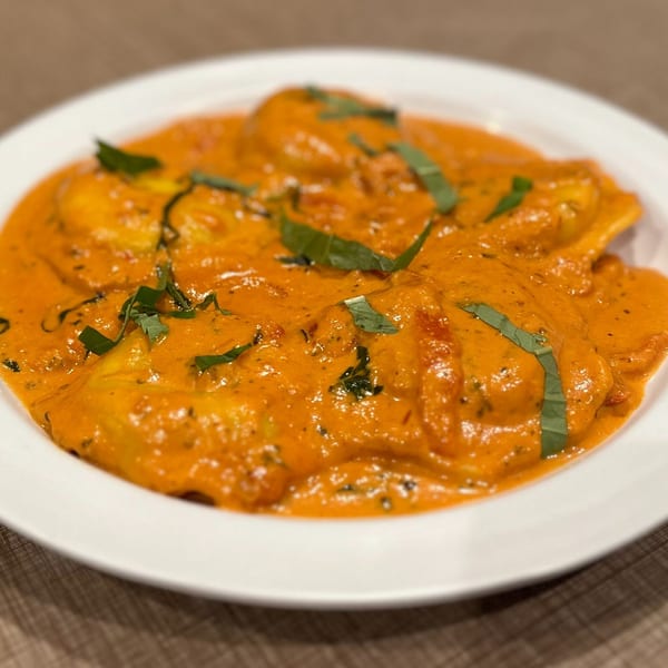 Ravioli pasta covered in a creamy orange sauce, garnished with fresh basil leaves.