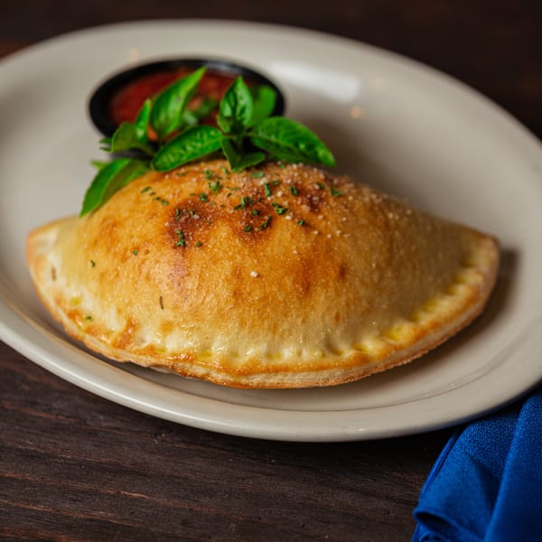 Golden-brown calzone with herbs and parmesan, served with a side of marinara sauce and fresh basil.