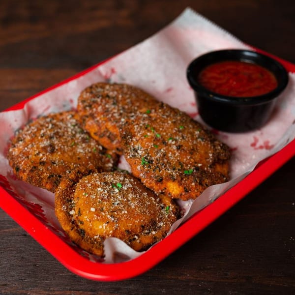 Three golden-brown fried ravioli, sprinkled with cheese and herbs, served with a side of marinara sauce.