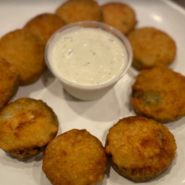 Golden-brown fried pickles arranged in a circle around a small cup of creamy dipping sauce.