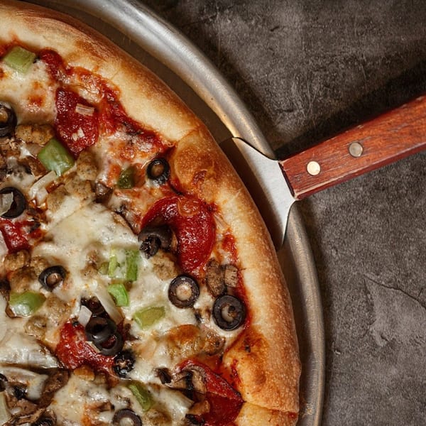 A Primo Brothers Pizza with pepperoni, sausage, olives, and green peppers on a metal pan.