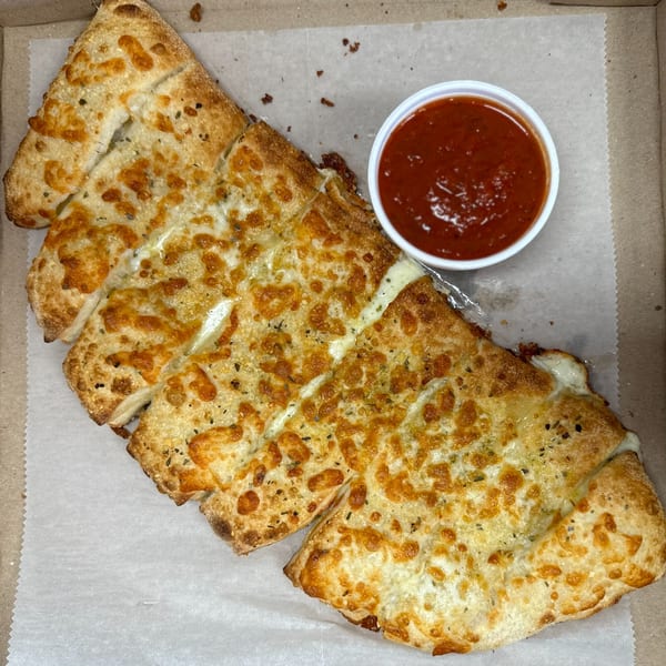 Primo Brothers Pizza garlic knots, cut into strips, with melted cheese and a side of marinara sauce.