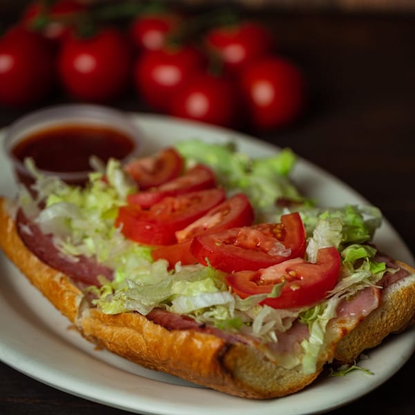 A Primo Brothers Pizza sub sandwich with lettuce, tomatoes, and meat, served with a side of sauce.